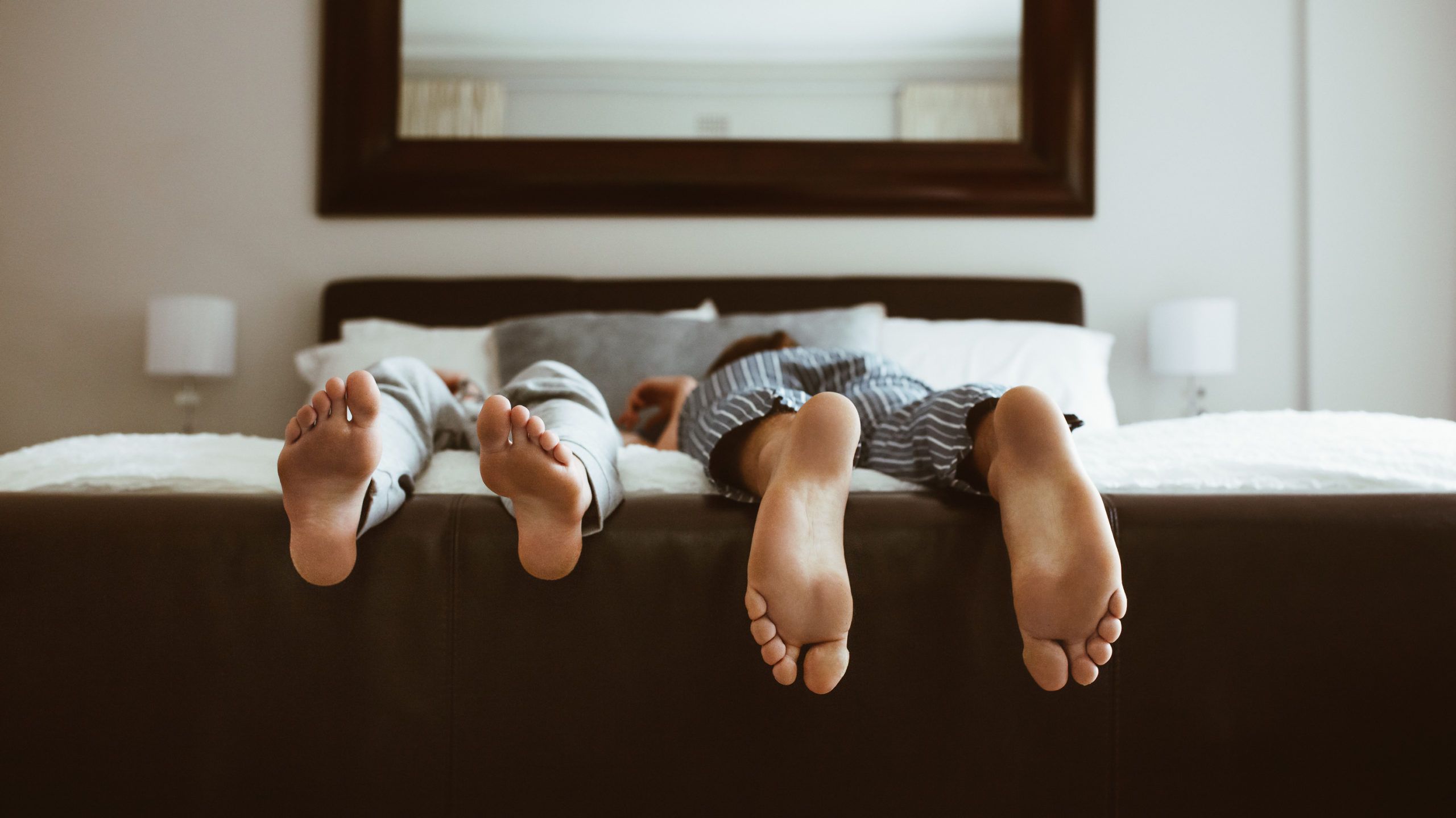 child laying down in bed with their feet over the bed